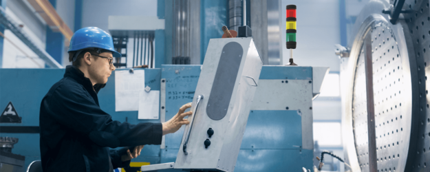 Ein Mann mit Sicherheitshelm und Brille bedient eine Maschine, auf der eine Signalleuchte steht.