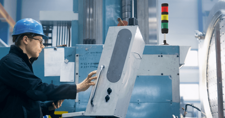 Ein Mann mit Sicherheitshelm und Brille bedient eine Maschine, auf der eine Signalleuchte steht.